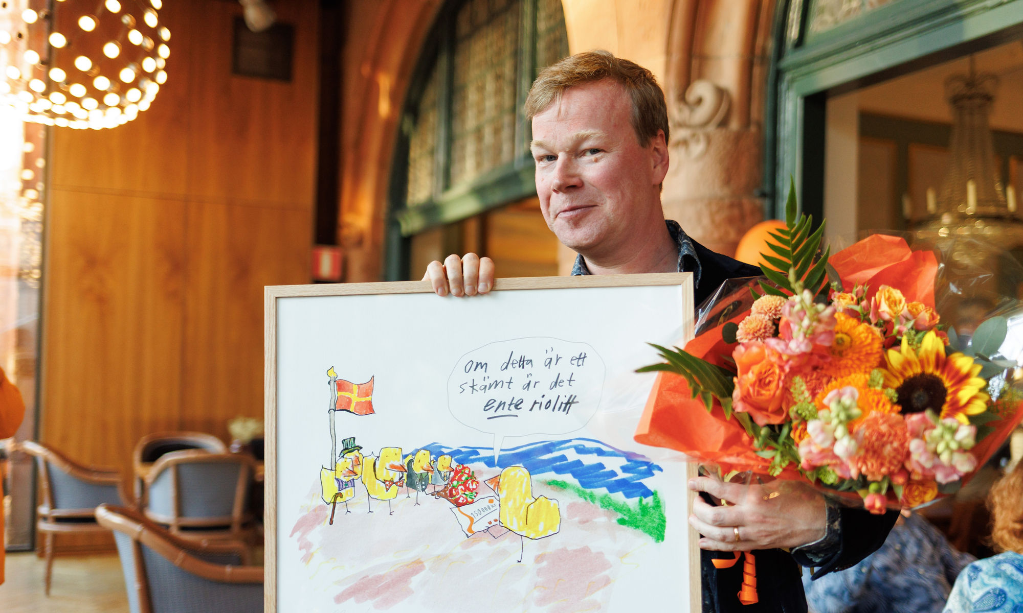 Johan Glans holding up a painting and flowers.
