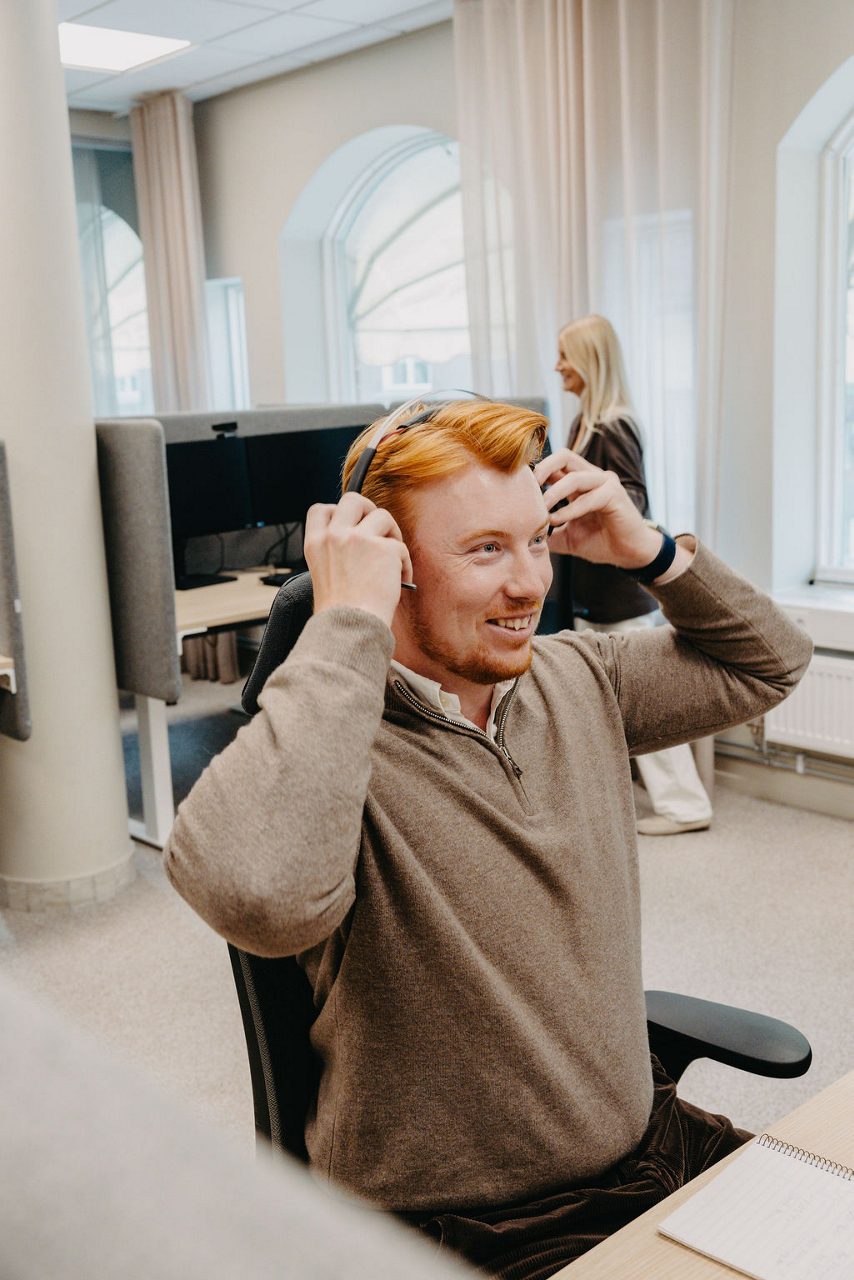 Man på kontor sätter på sig ett headset och ler.