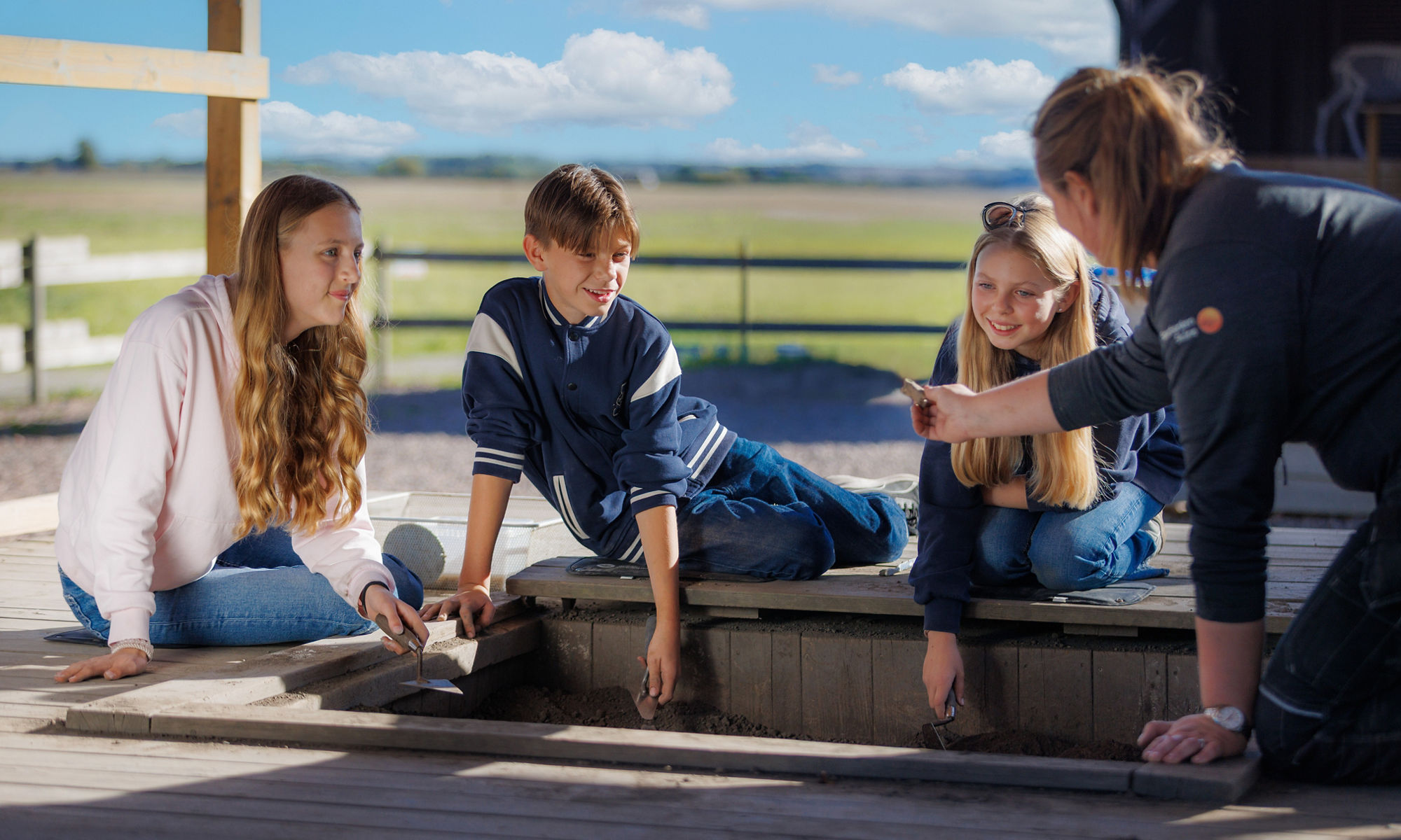 Tre barn sitter tillsammans med en arkeolog och tittar på ett fynd.