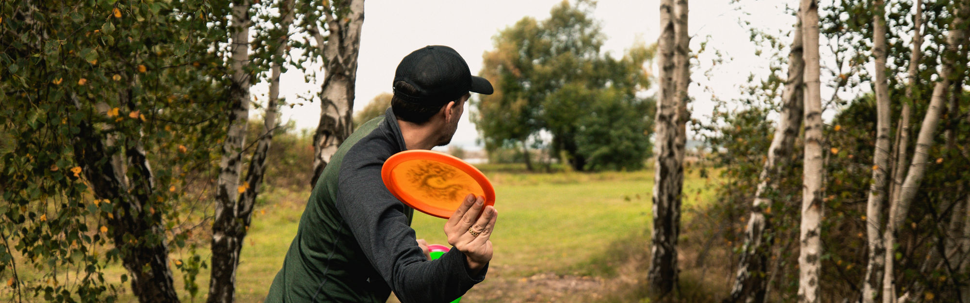 Man kastar en orange discgolf genom skogen