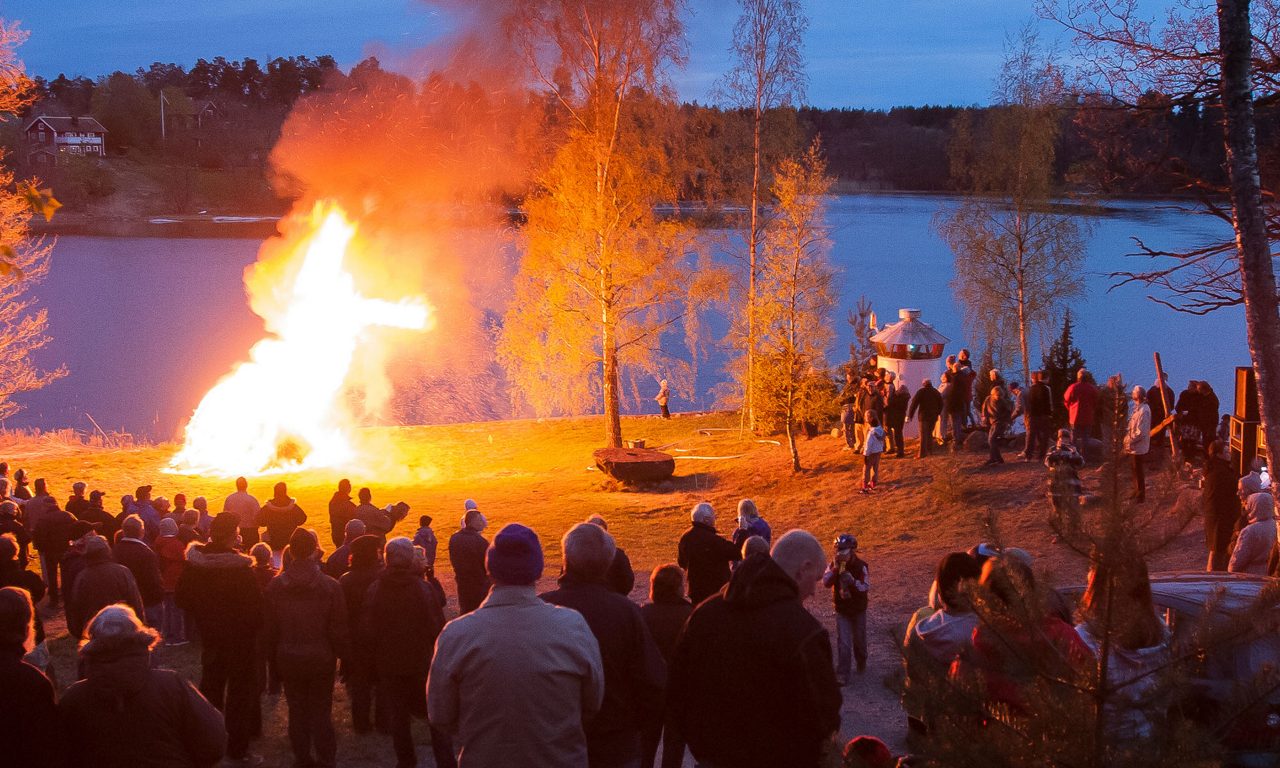 Människor som står och tittar på en brasa utomhus vid en sjö