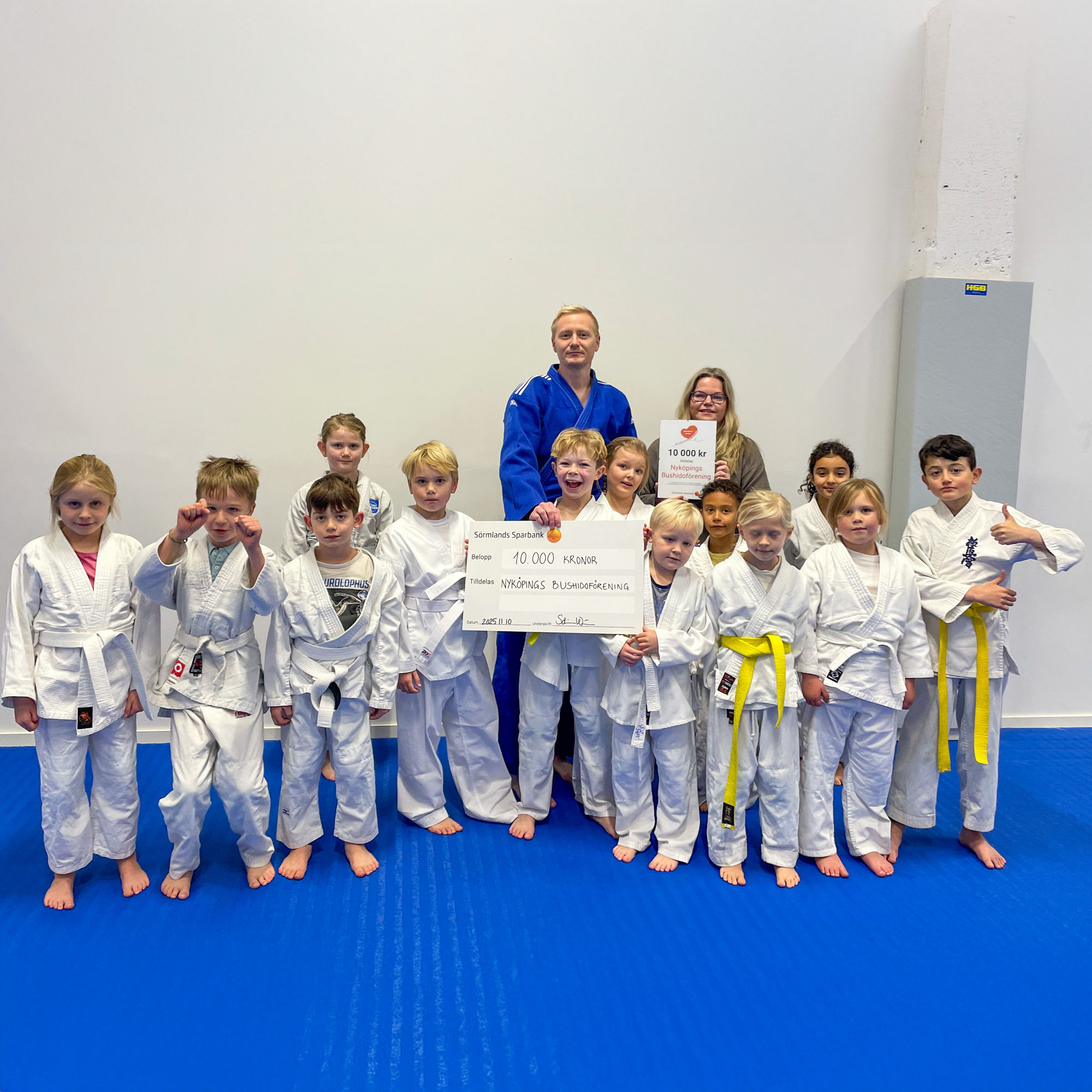 En grupp barn och två vuxna håller i en check och ett diplom.