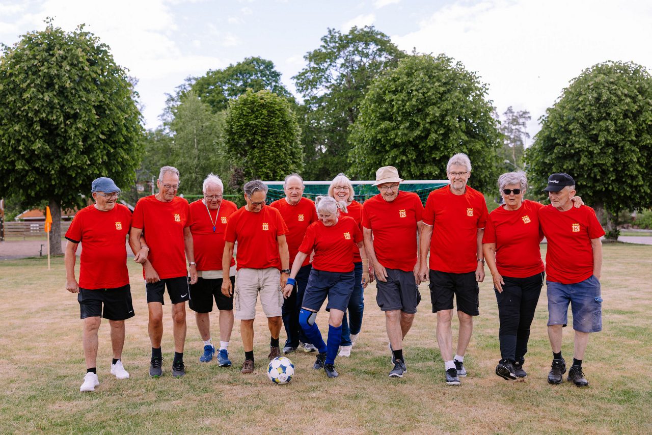 Elva pigga och glada pensionärer på fotbollsplanen i Fröseke iklädda Kronofrs IF:s röda fotbollströjor. 