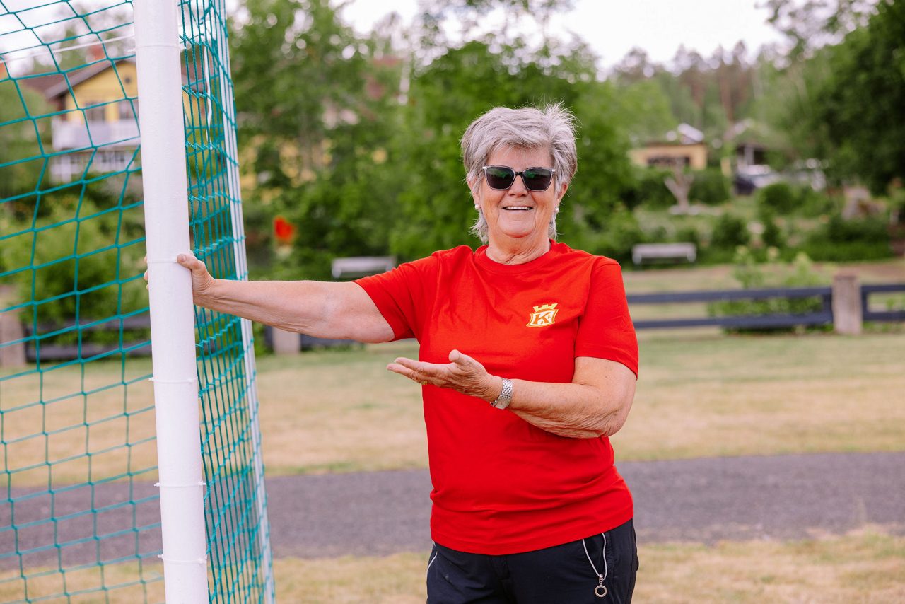 Birgitta Ek som står vid ett fotbollsmål iklädd en röd fotbollströja från Kronofors IF och med solglasögon. 