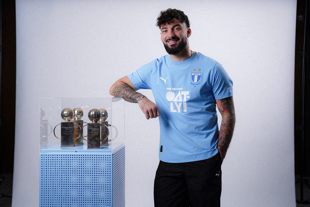 En man i MFF-tröja lutar sig mot en glasbox med troféer i.