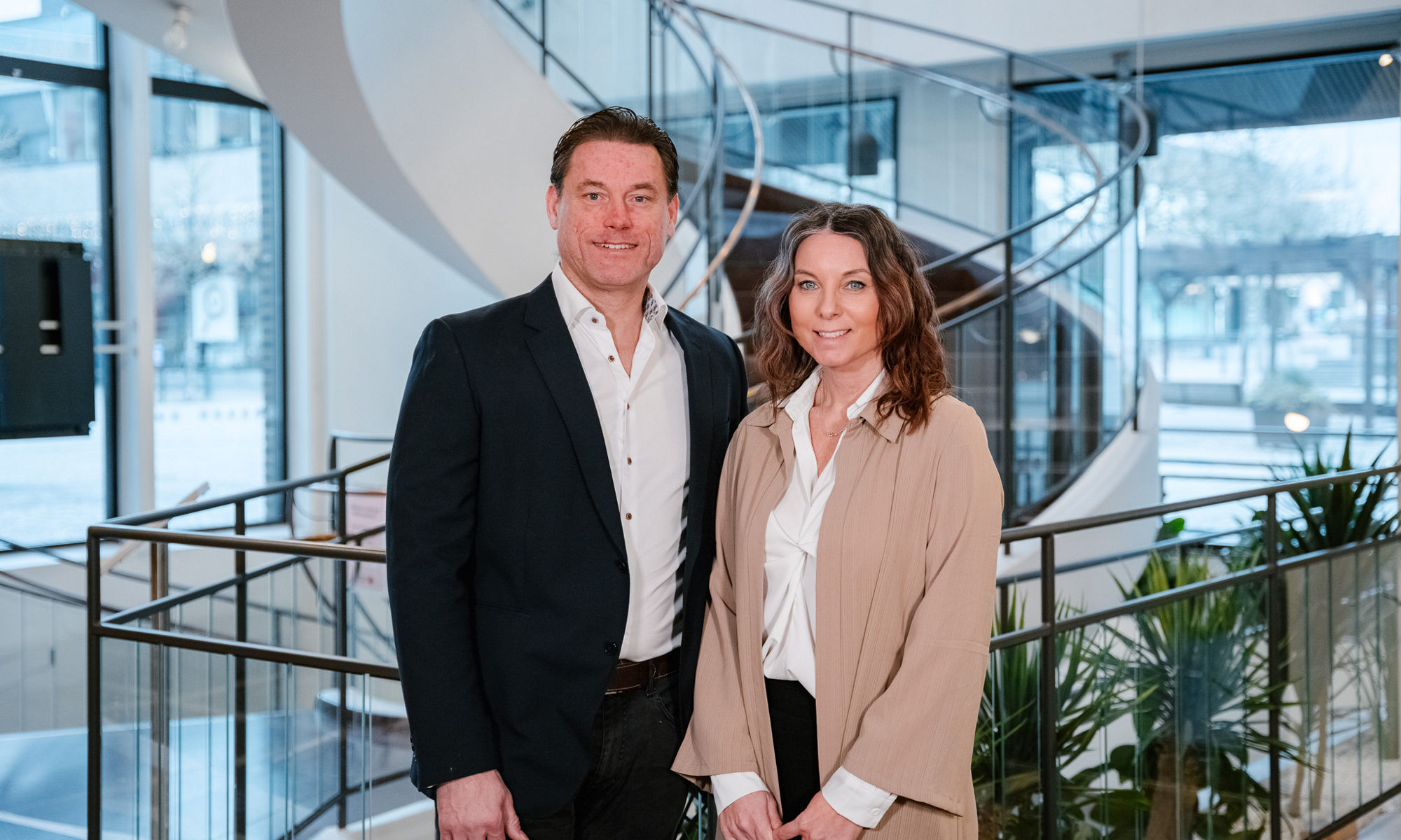 Två personer står bredvid varandra framför en sprialtrappa inne i en kontorsbyggnad