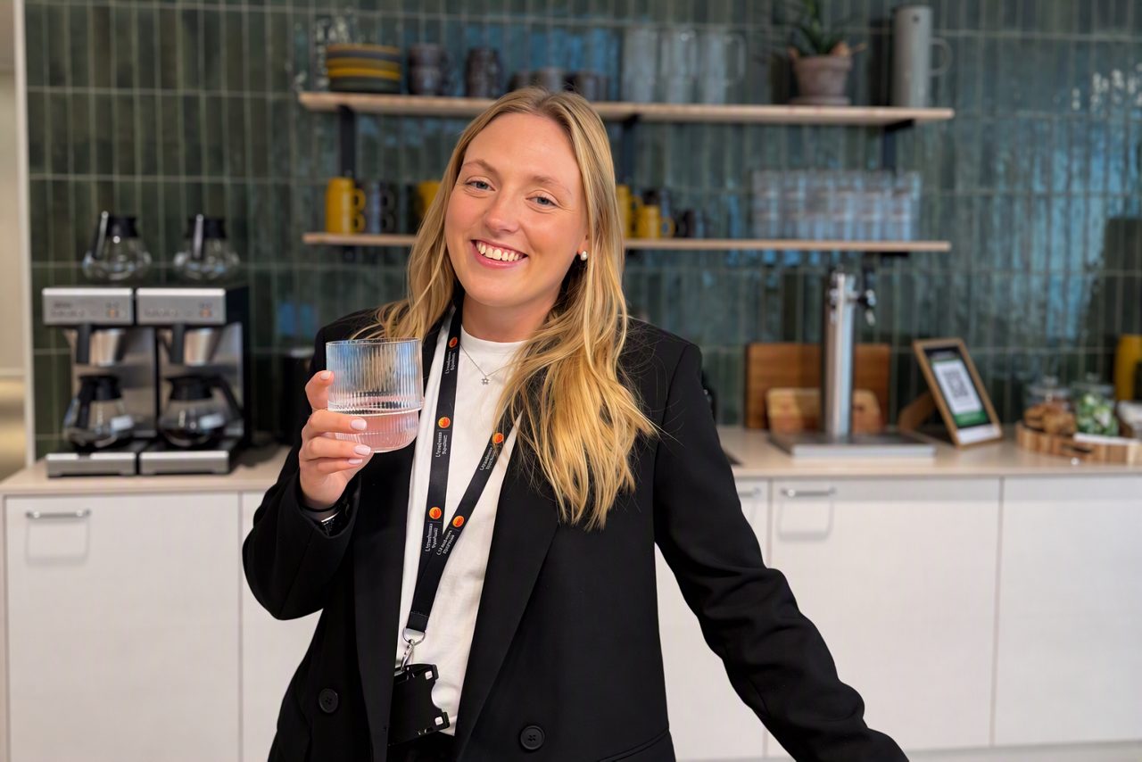 Ung kvinna står i ett cafe, tittar in i kameran och ler