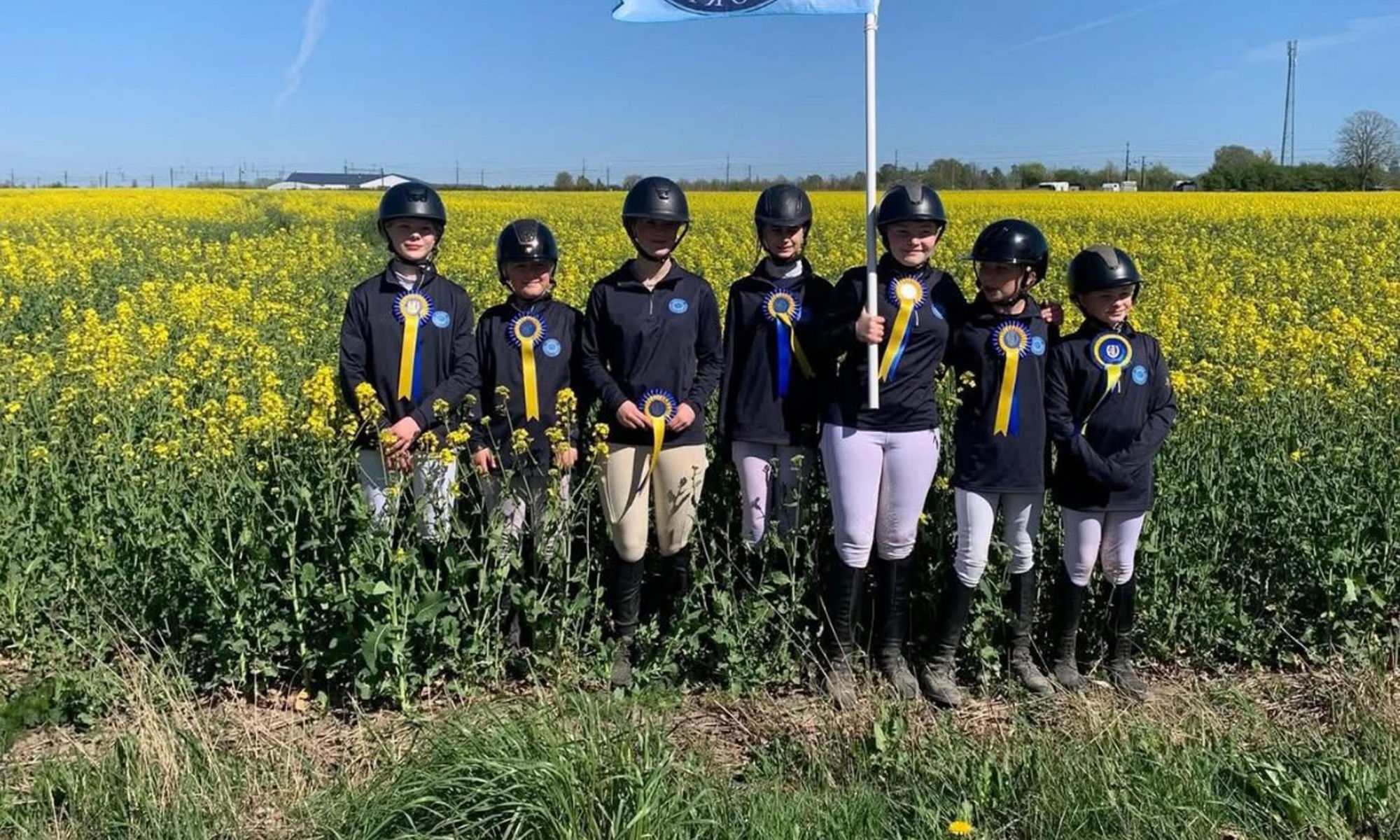 Ryttare som står vid ett fält och håller en flagga.