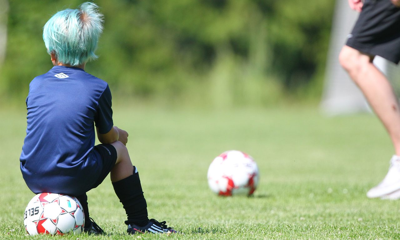 Barnet sitter på sin fotboll på fotbollsplanen.