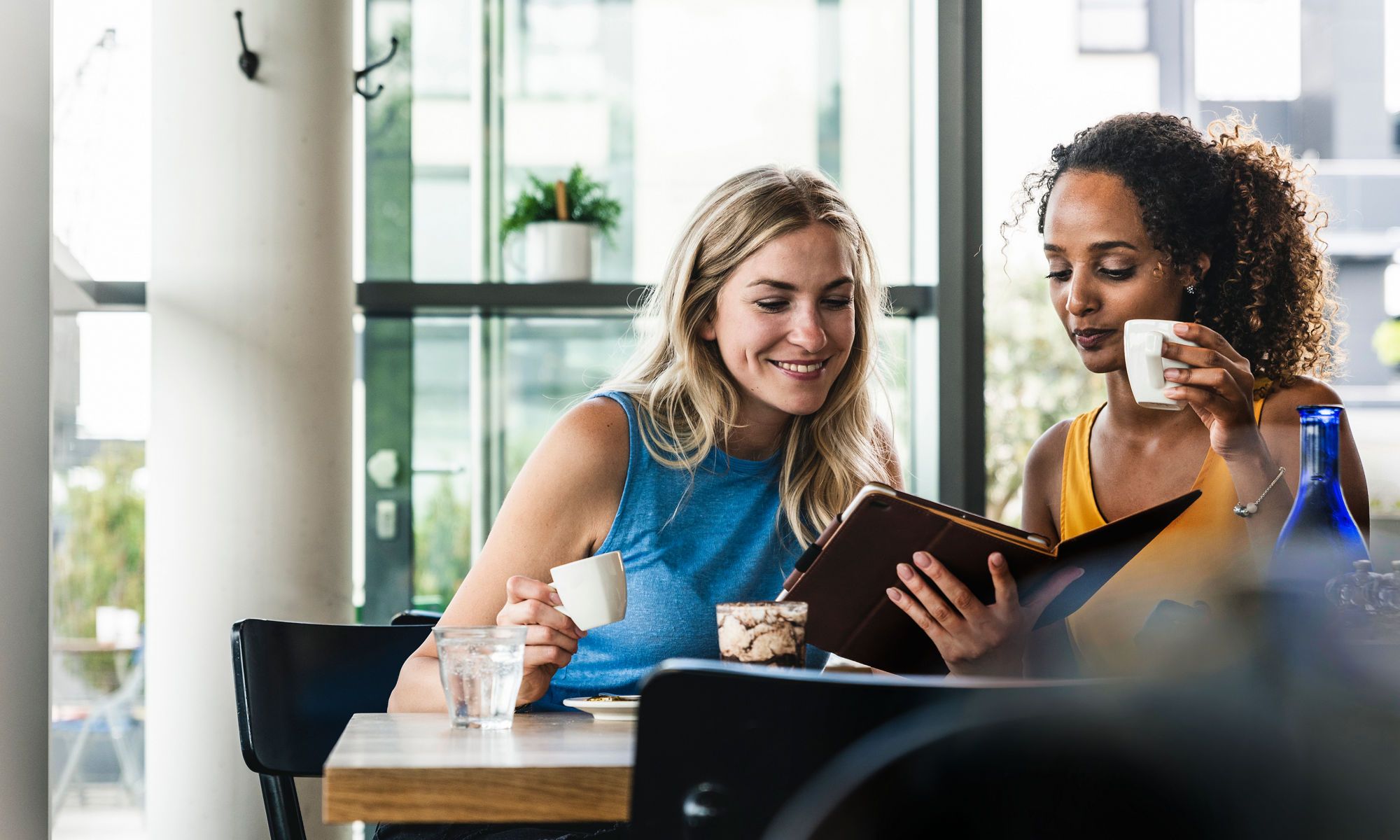 Two young women in a coffee shop, reading and having a coffee