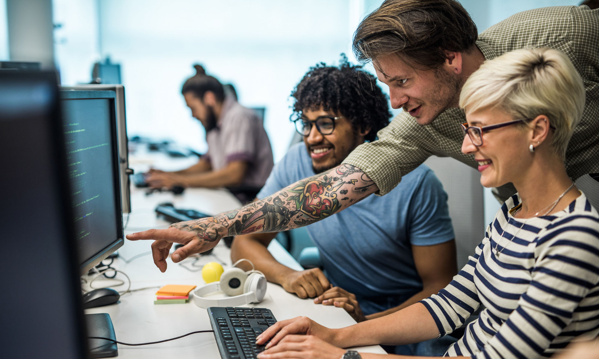 Tre unga personer tittar på en datorskärm på ett kontor.