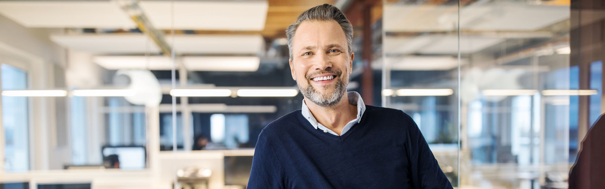 Man standing in office, smiling towards the camera and holding glasses