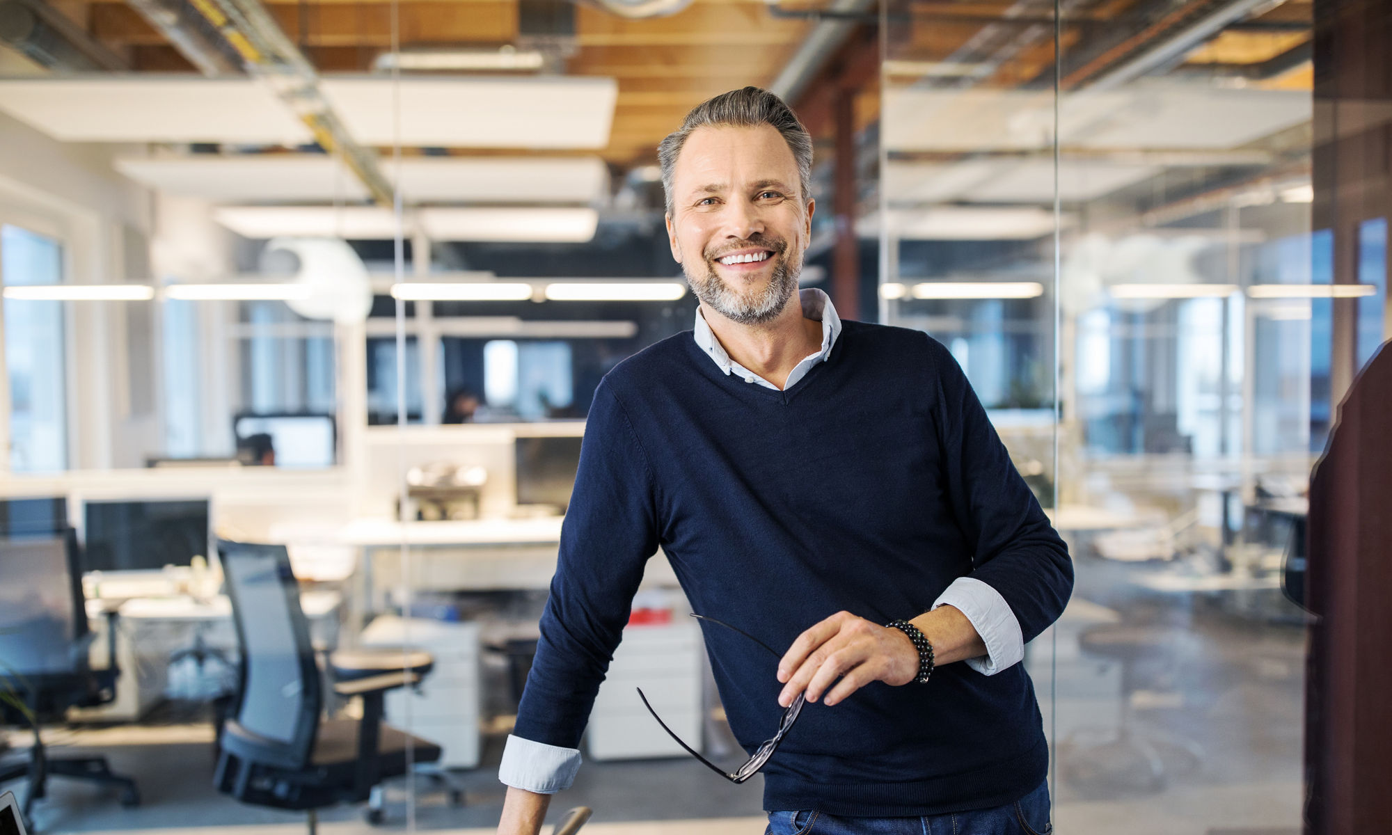 Man standing in office, smiling towards the camera and holding glasses