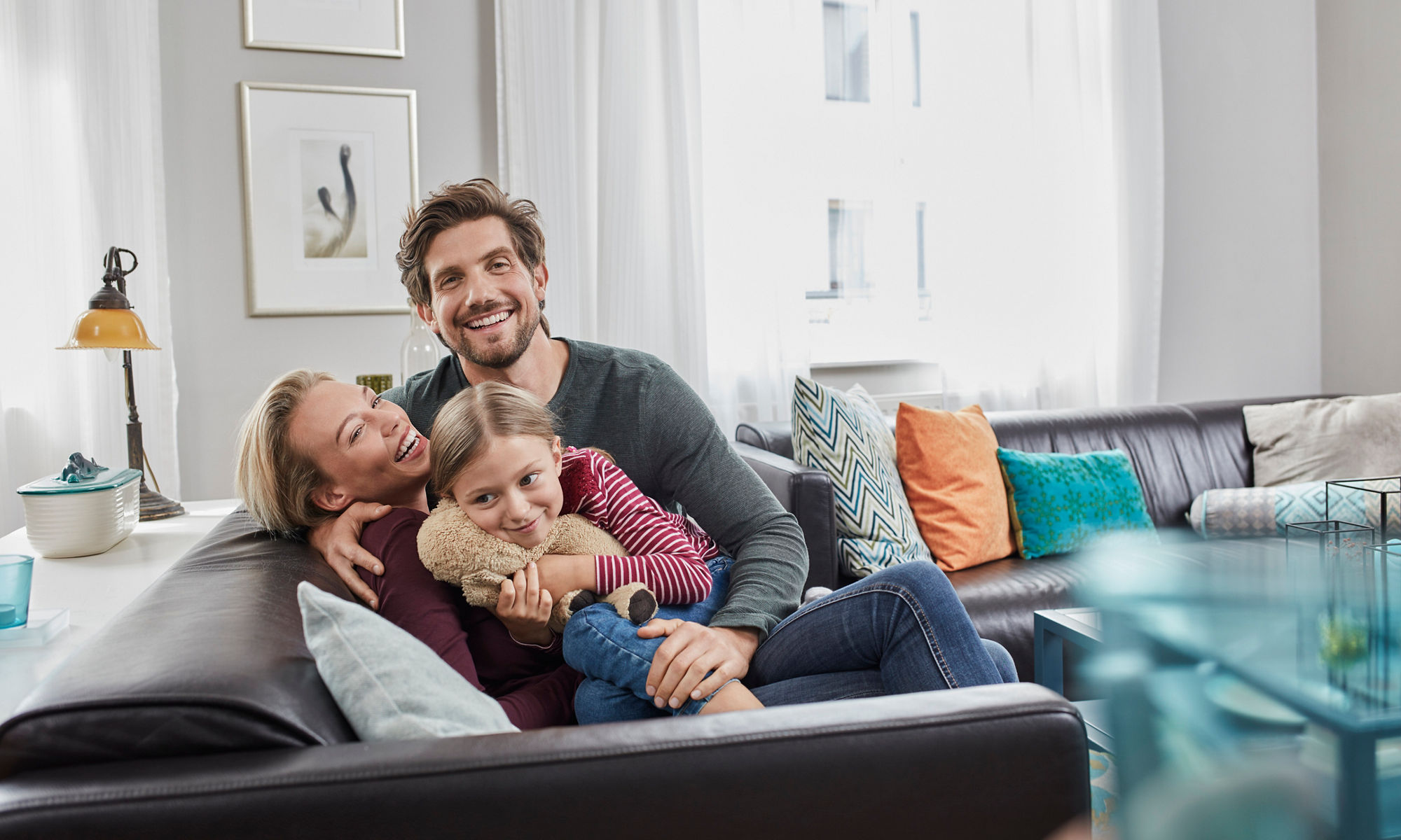 Två glada vuxna och ett barn sitter och håller om varandra i en soffa