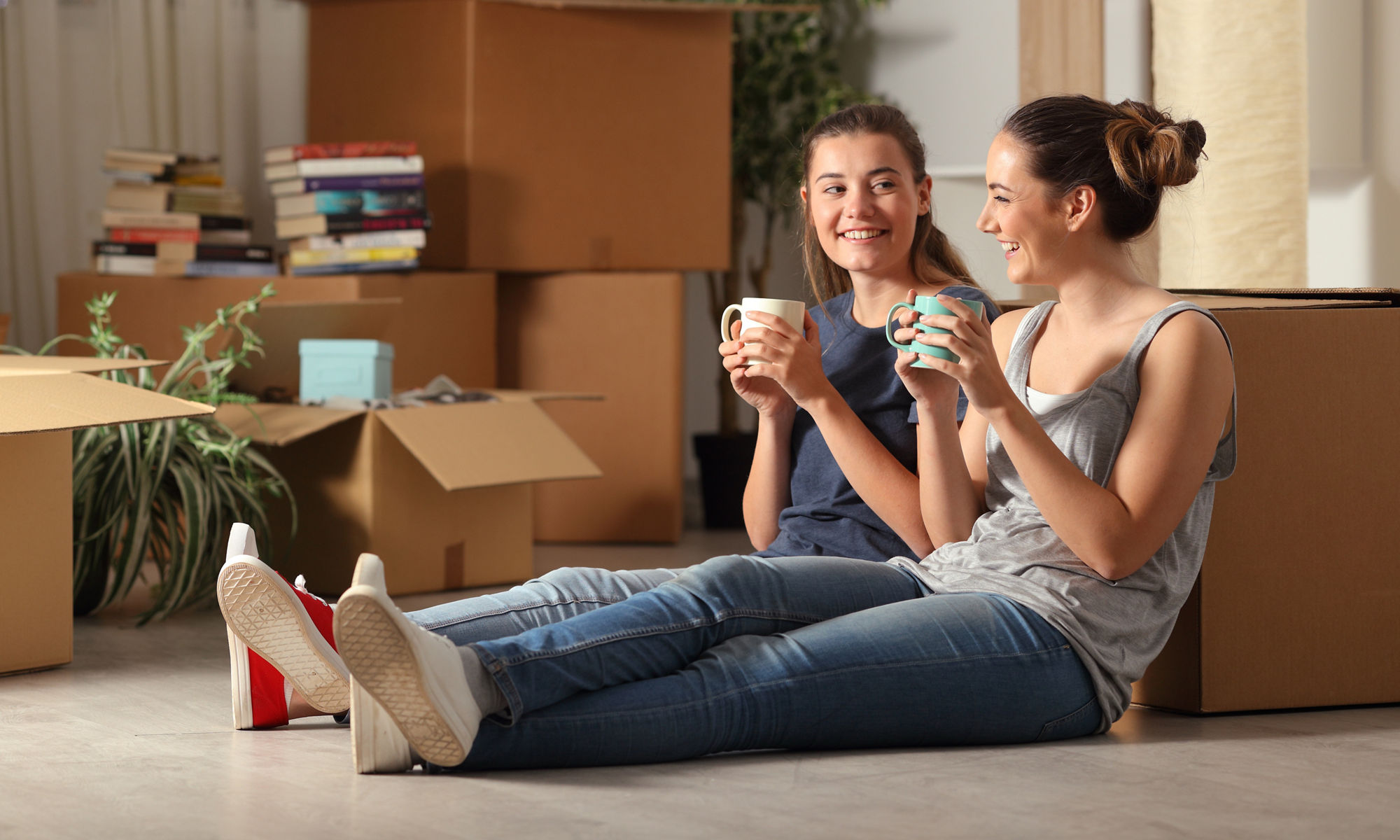 Two smiling women sitting on the floor of a room with moving boxes