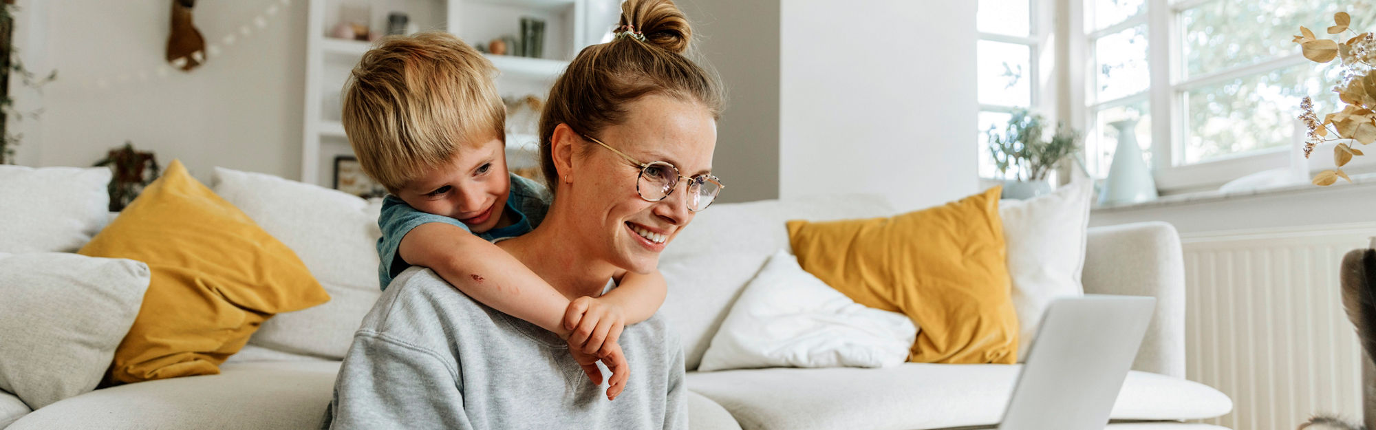 Kvinna och barn sitter i vardagsrummet med en bärbar dator, ler och kramas