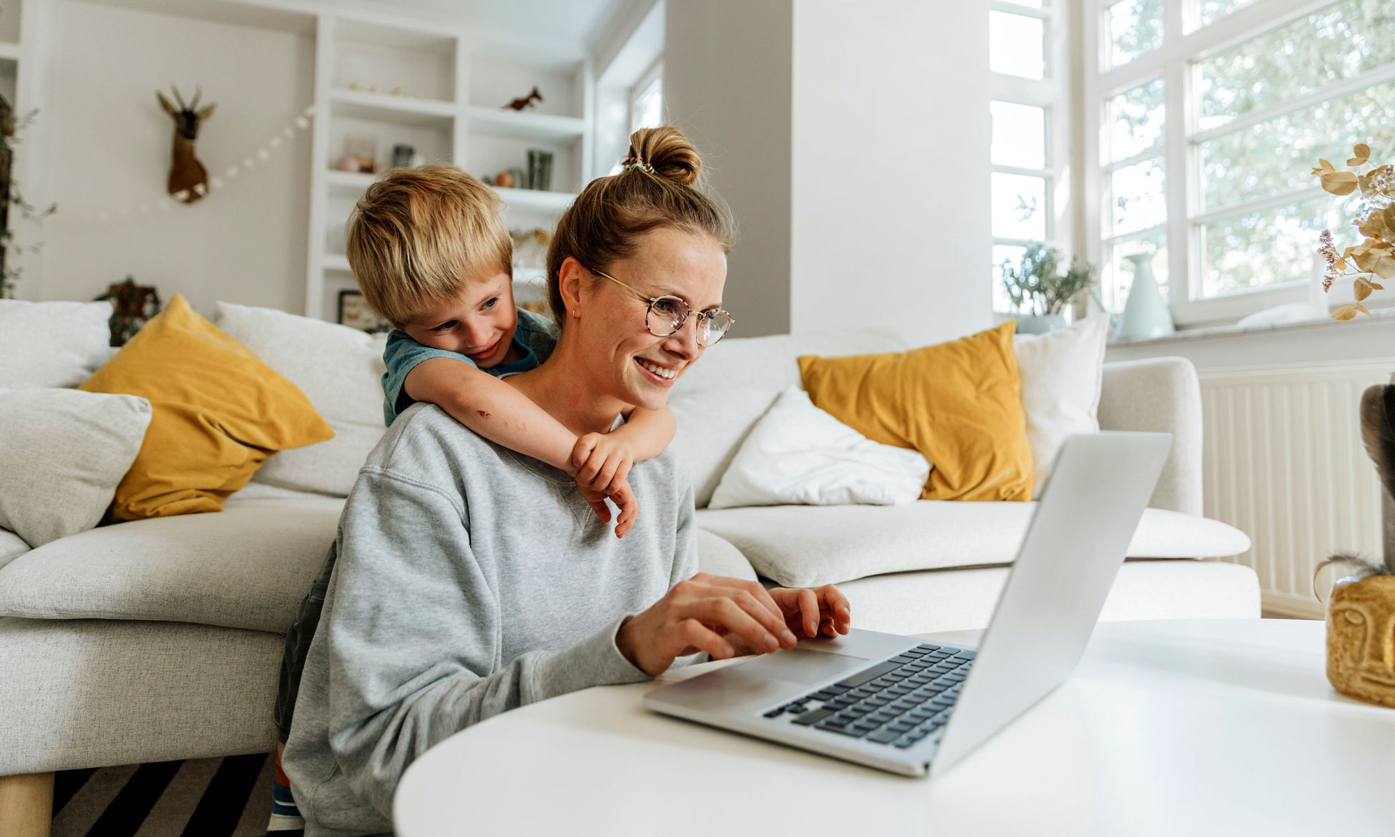 Kvinna och barn sitter i vardagsrummet med en bärbar dator, ler och kramas