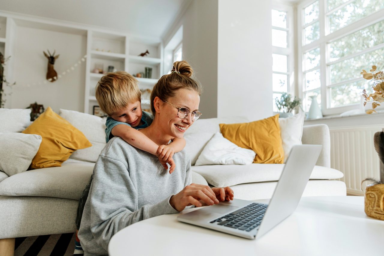 Kvinna och barn sitter i vardagsrummet med en bärbar dator, ler och kramas