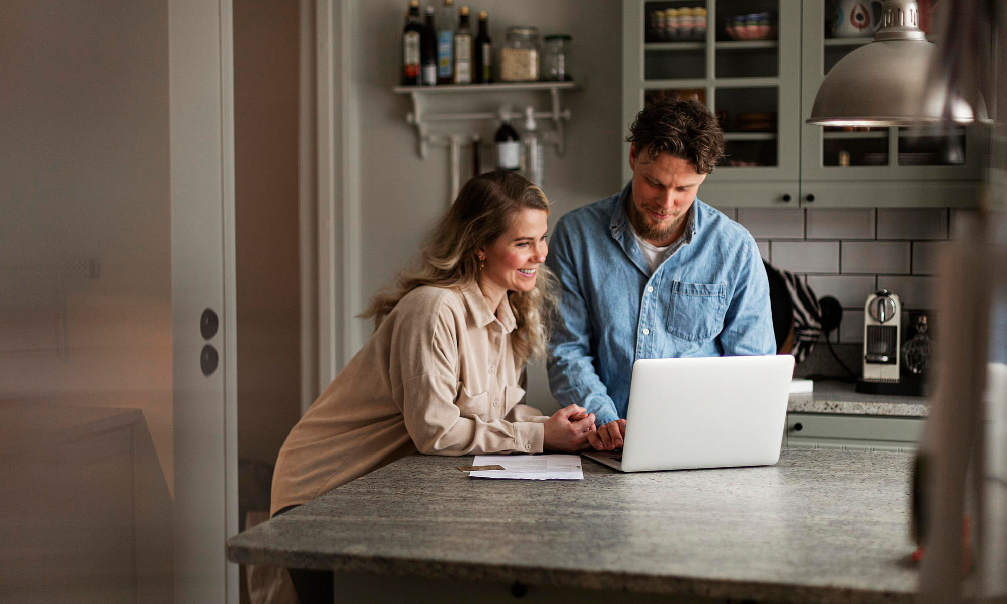 En kvinna och en man står vid köksbordet och tittar i en bärbar dator