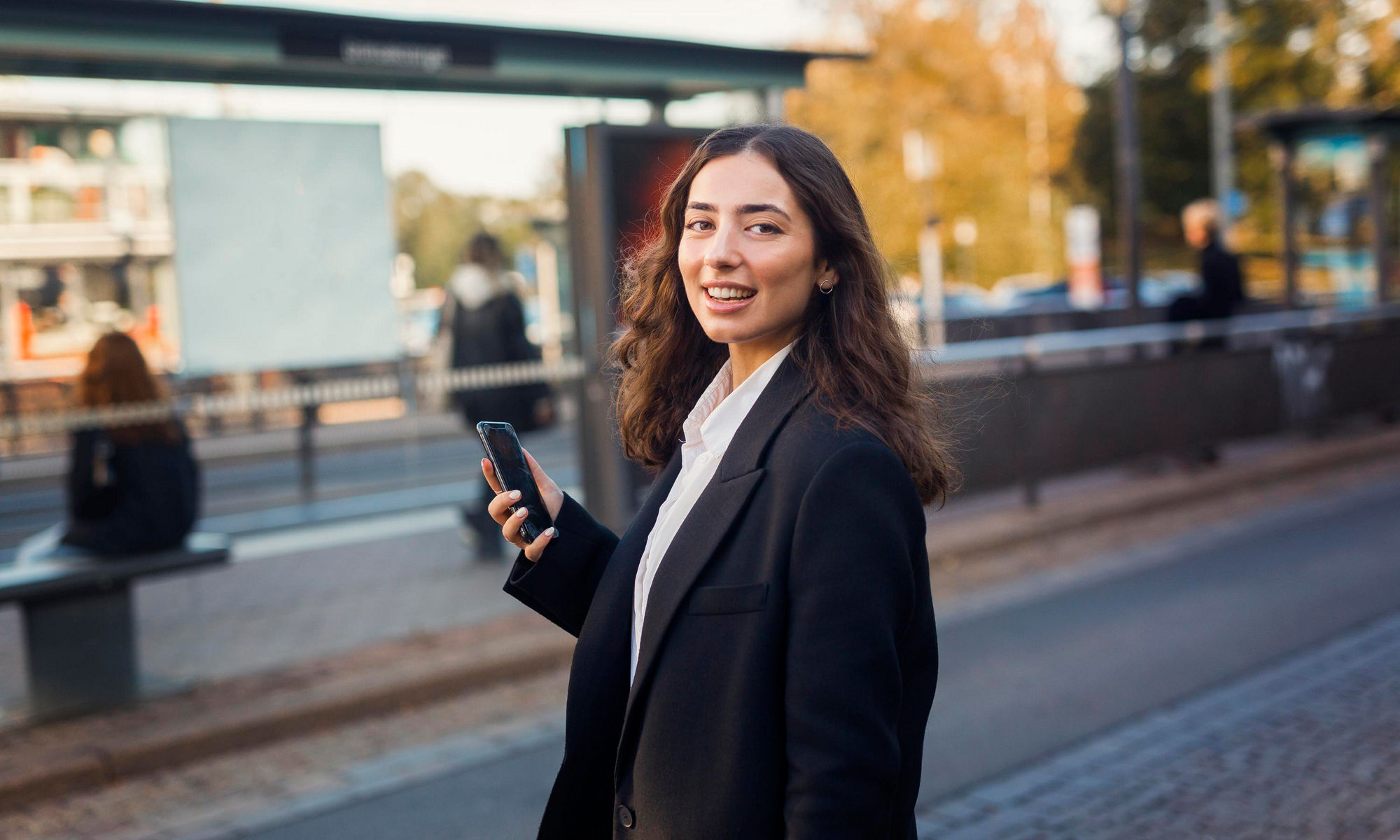 En kvinna vid en busshållplats håller i en mobiltelefon