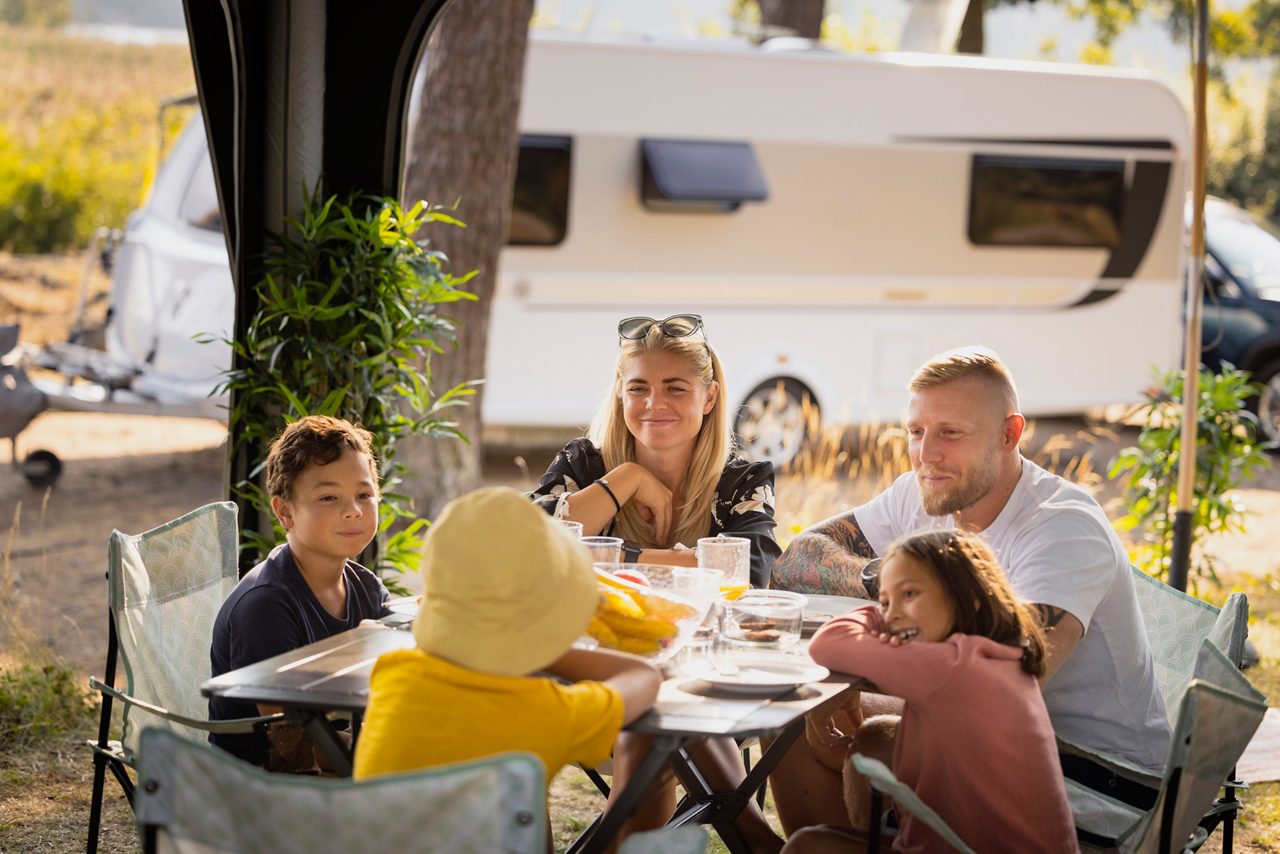 Vuxna och barn sitter på en camping och äter mat utomhus