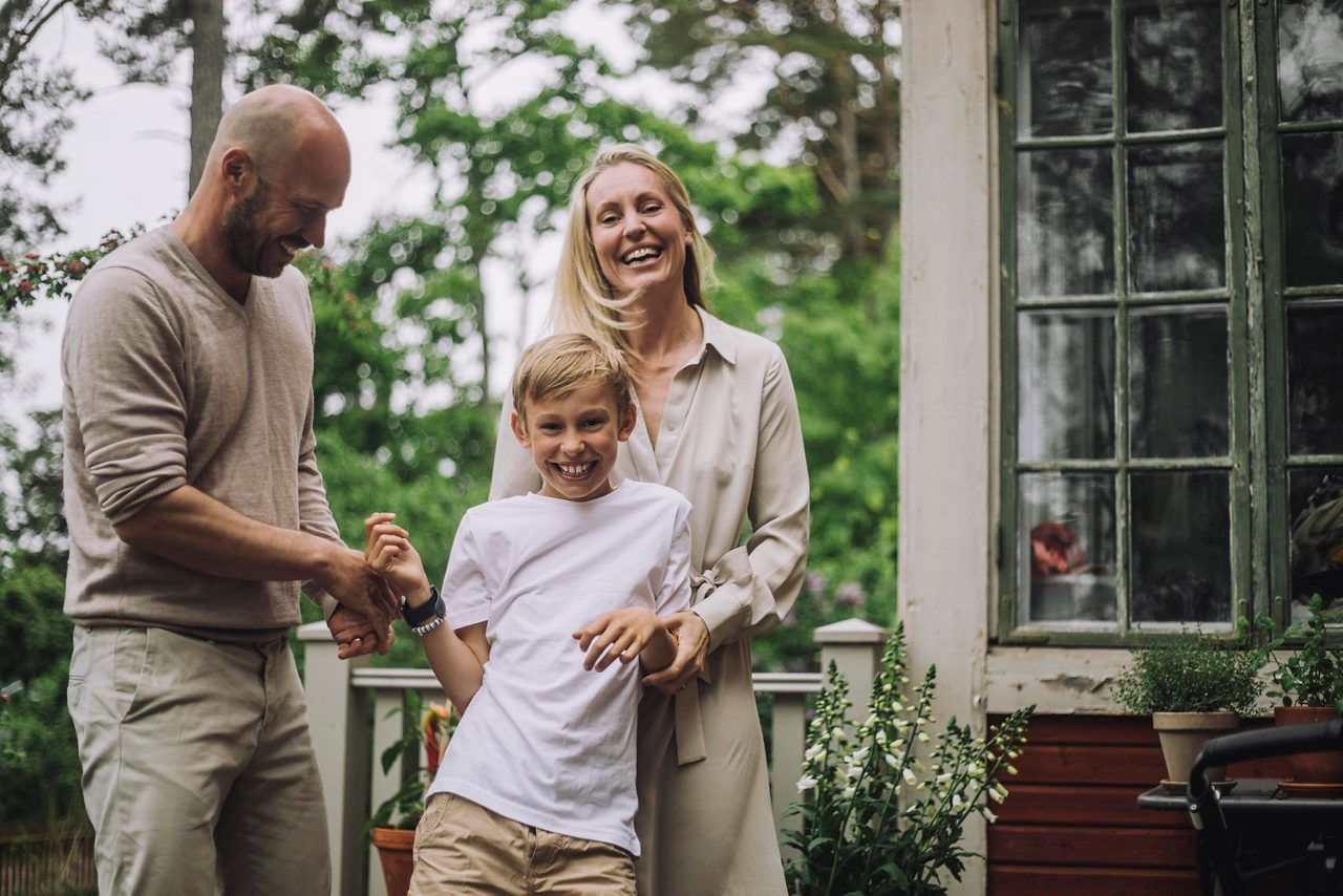 En man och en kvinna och en liten pojke står utanför ett hus och ler.