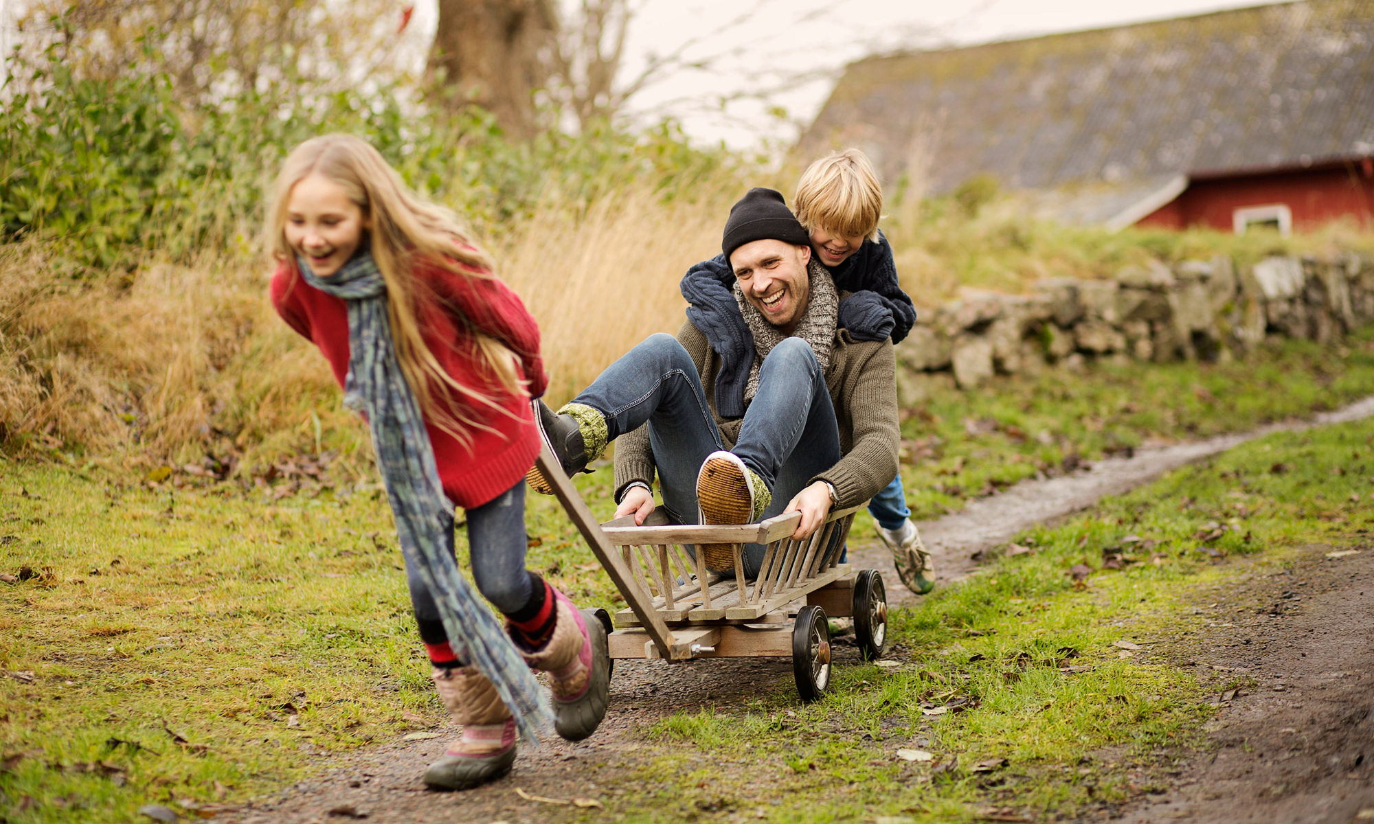 Two kids driving a man in a cart, all laughing