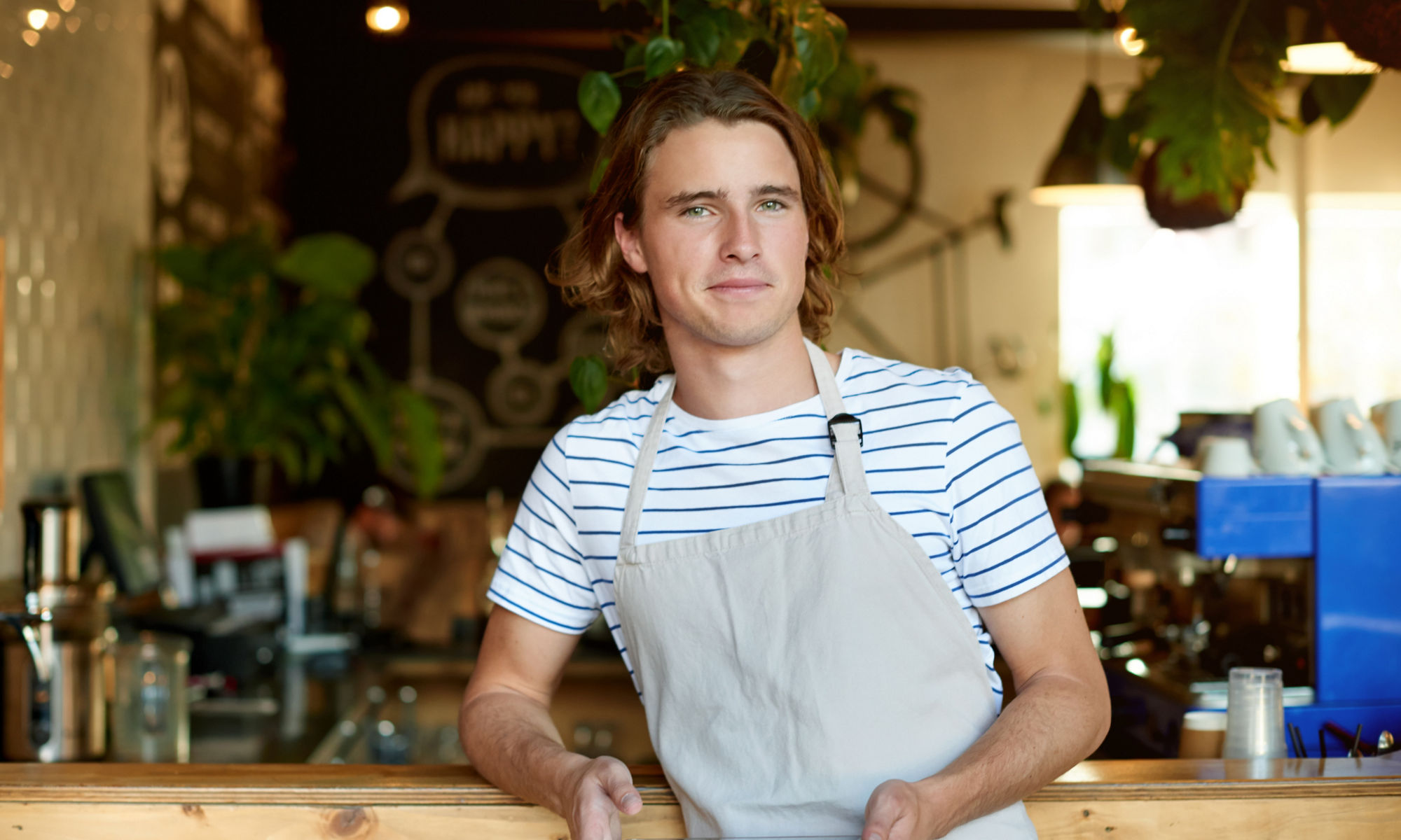 Ung man jobbar på ett café, står och håller i en surfplatta