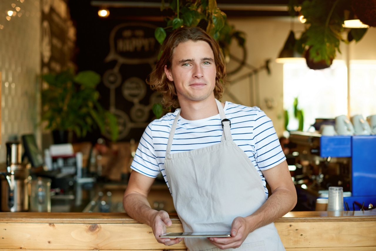 Young man working in a coffee shop, holding a digital tablet