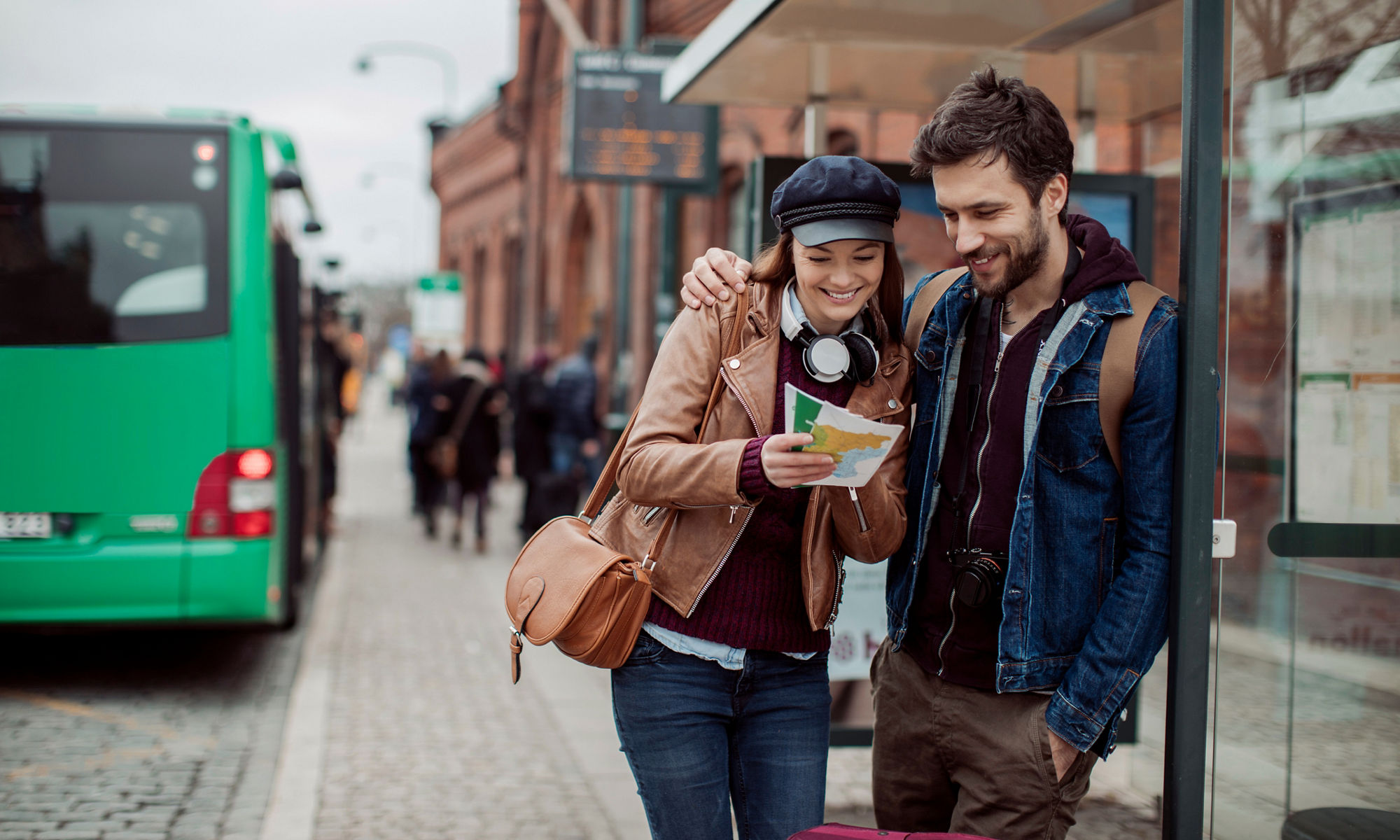 Man och kvinna står på en busstation, tittar på en karta och ler