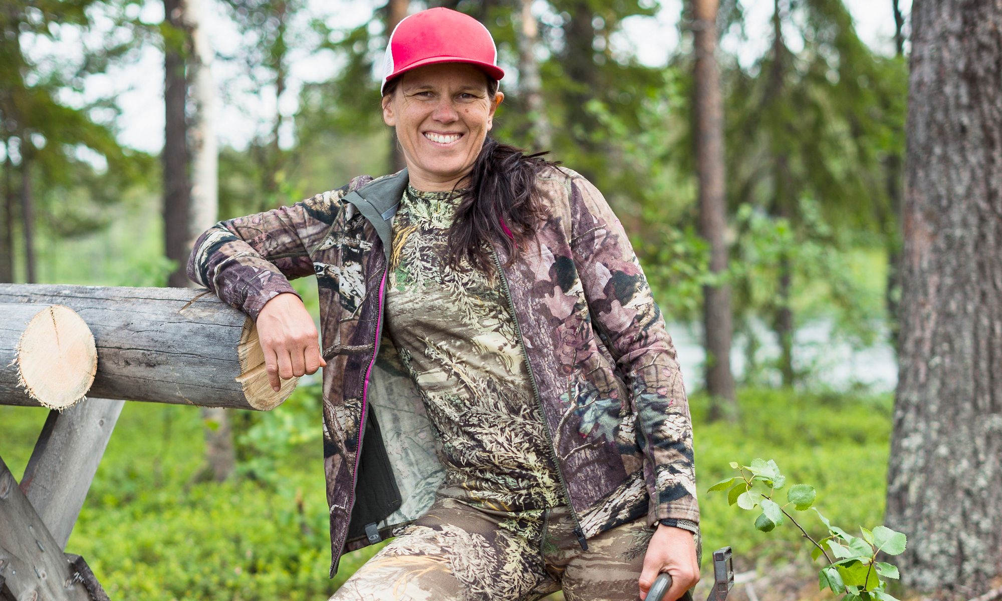 Leende kvinnlig skogshuggare står i skogen med en motorsåg i handen