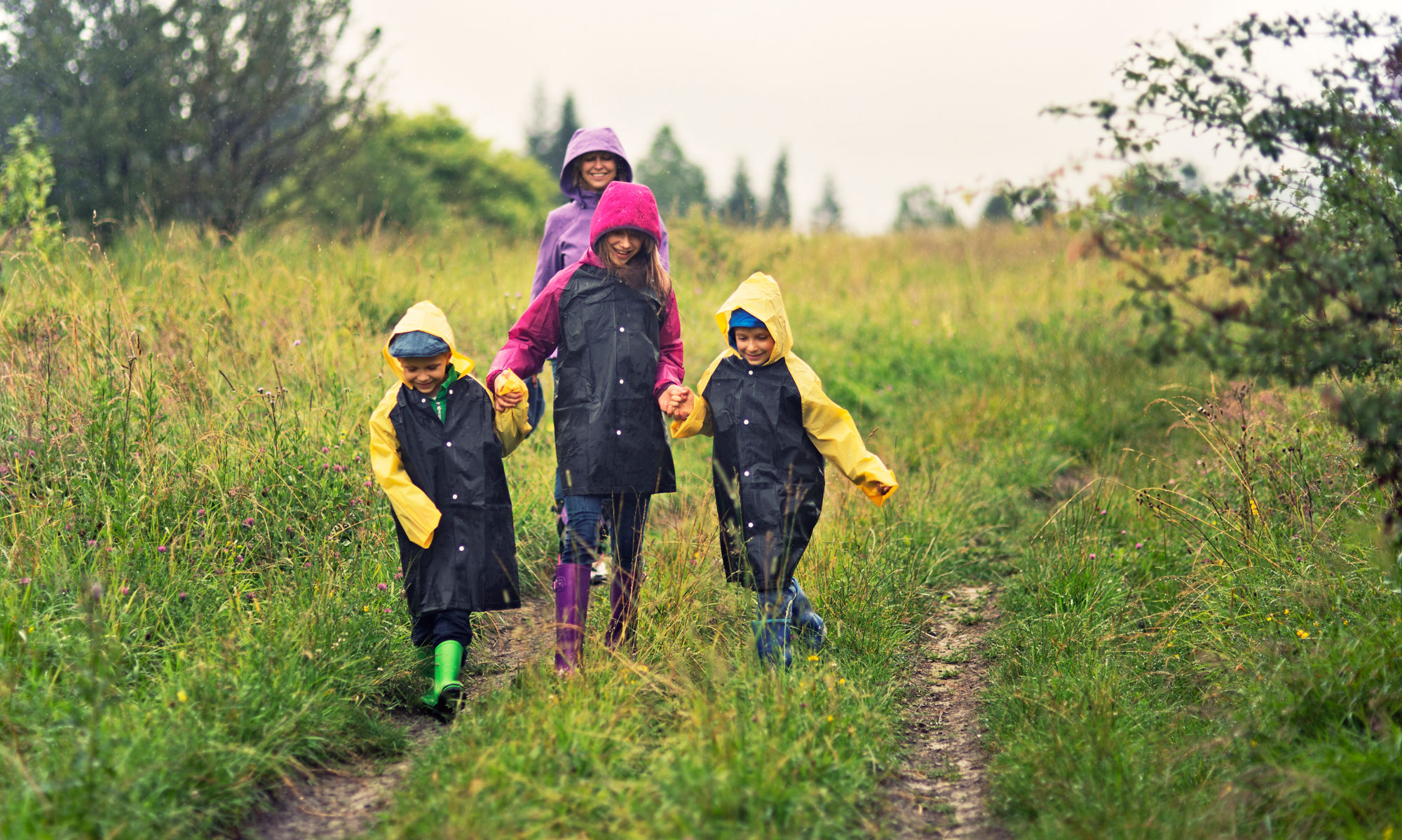 Adult and children walking outdoors in the grass, wearing raincoats