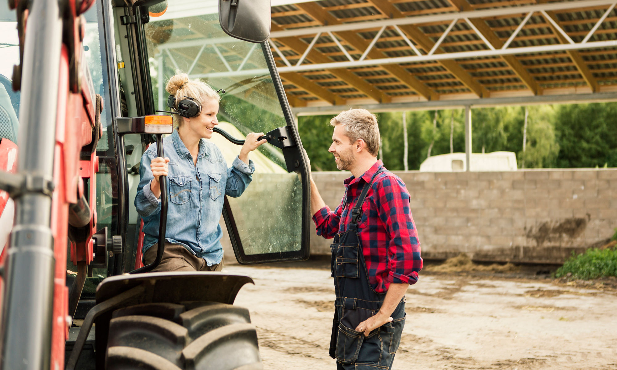 Två bönder tittar leendes på varandra bredvid en traktor