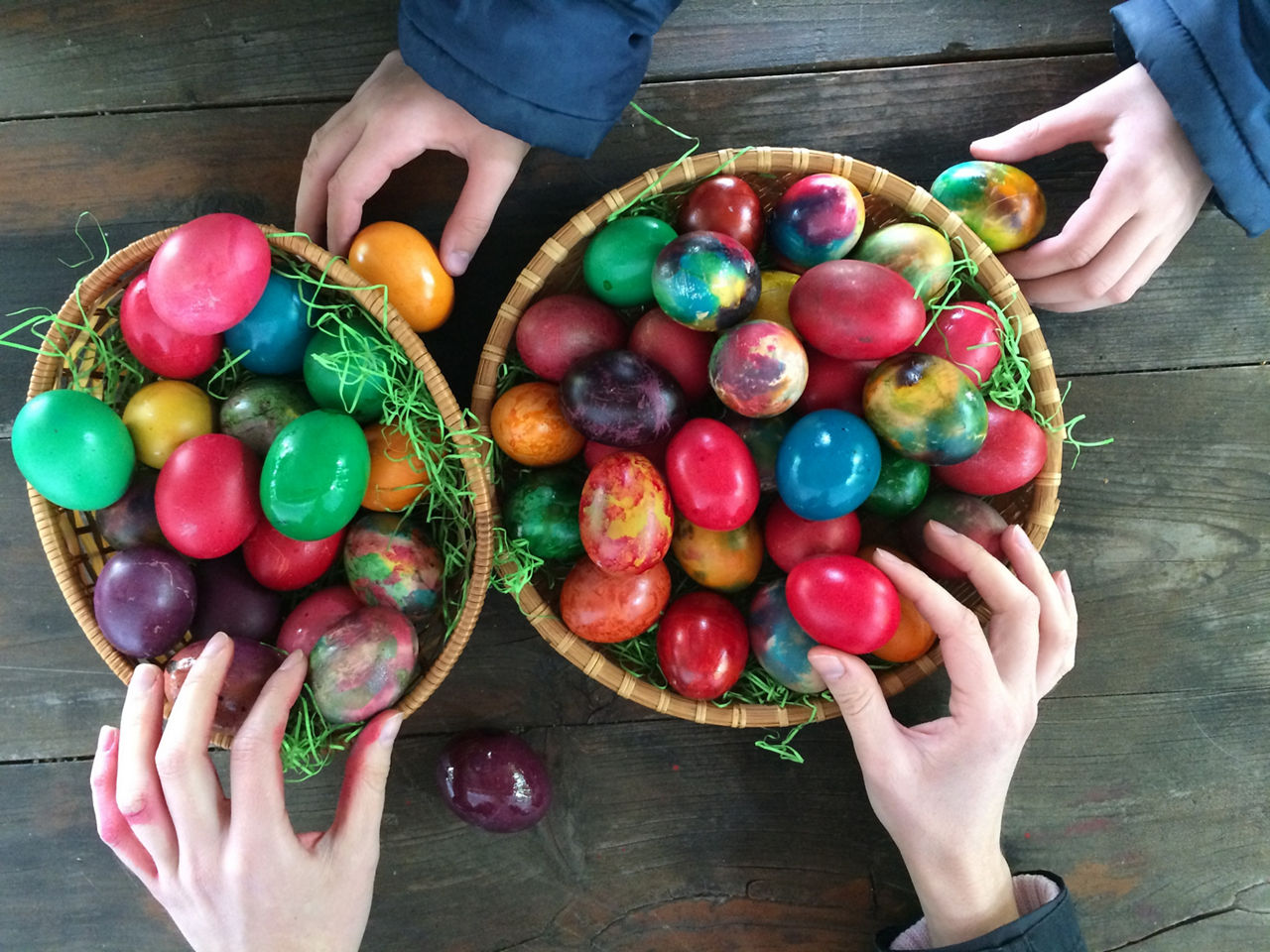 Two pair of hands touching Easter eggs in baskets