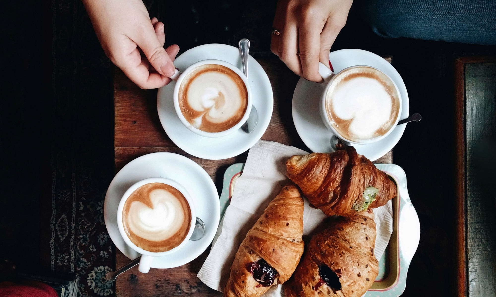 Händer som håller i kaffekoppar, croissanter ligger på bordet