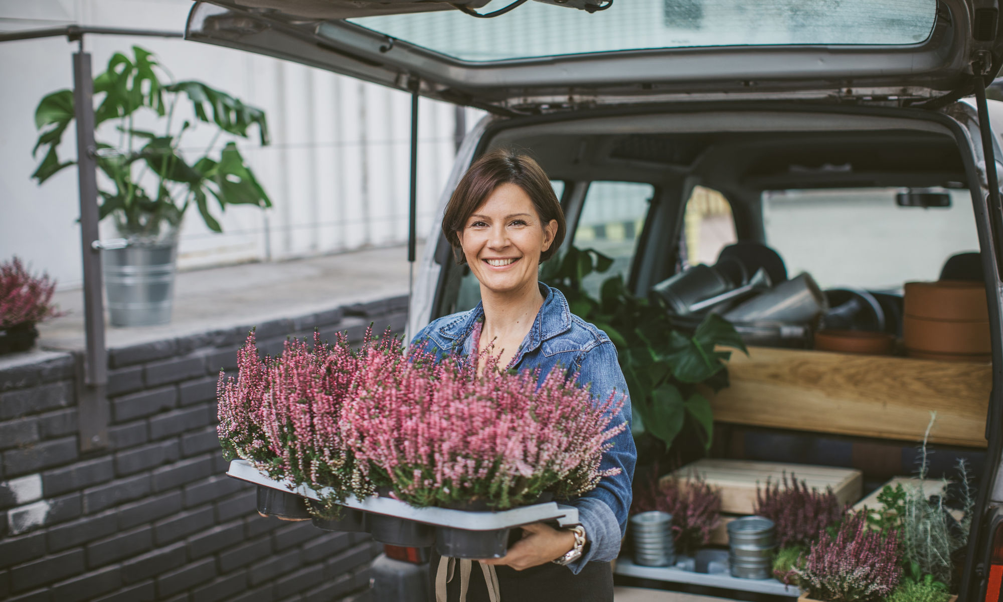 Leende kvinna fyller bagageutrymmet på en bil med blommor av olika sorter