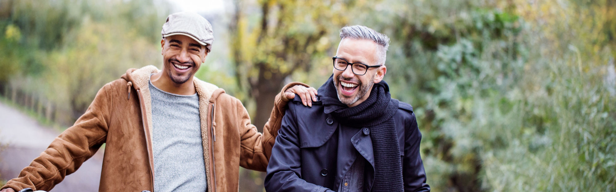 Two laughing men walking with their bicycles