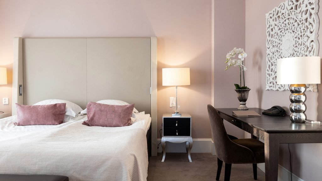 Ett fint hotellrum med rosa väggar, en stor säng, ett mörkbrunt skrivbord