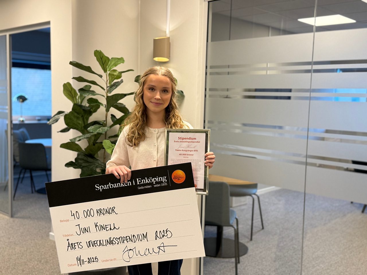 en ung kvinna ler mot kameran hållandes stor check och blombukett