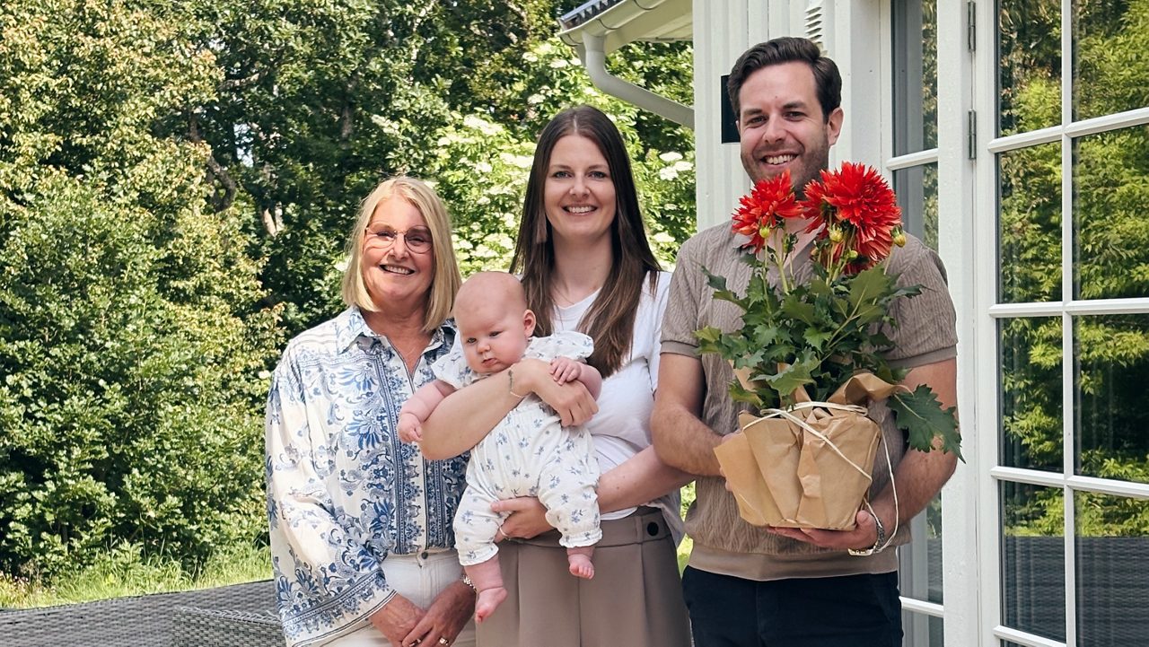 Tre personer och en bebis framför ett hus