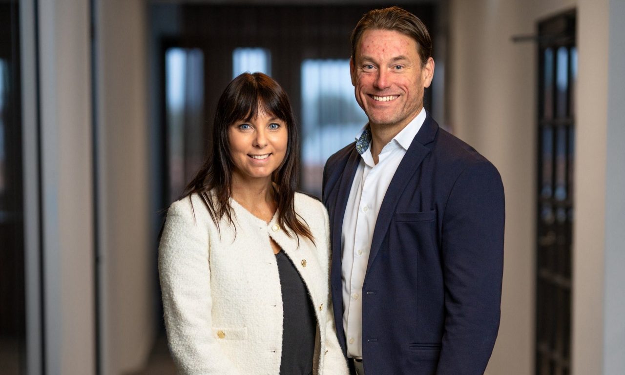 Leende kvinna och man poserar i kontorsmiljö med suddig bakgrund.