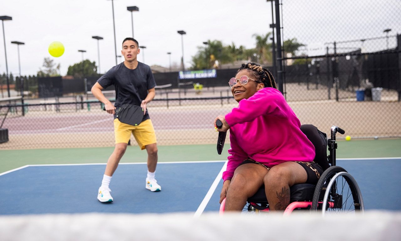 Ung kvinna med funktionsnedsättning spelar pickle ball med vän