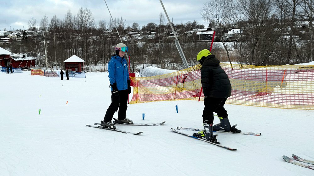 Bild på barn som åker slalom med hjälp av en skidlärare