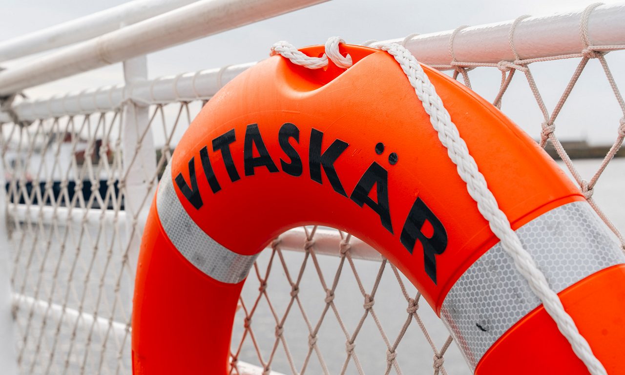 En orange livboj på däck med texten Vitaskär