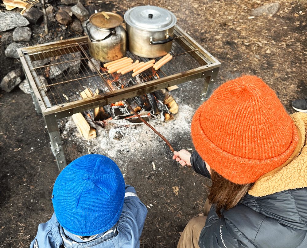 En kvinna och ett barn grillar korv utomhus över en eld
