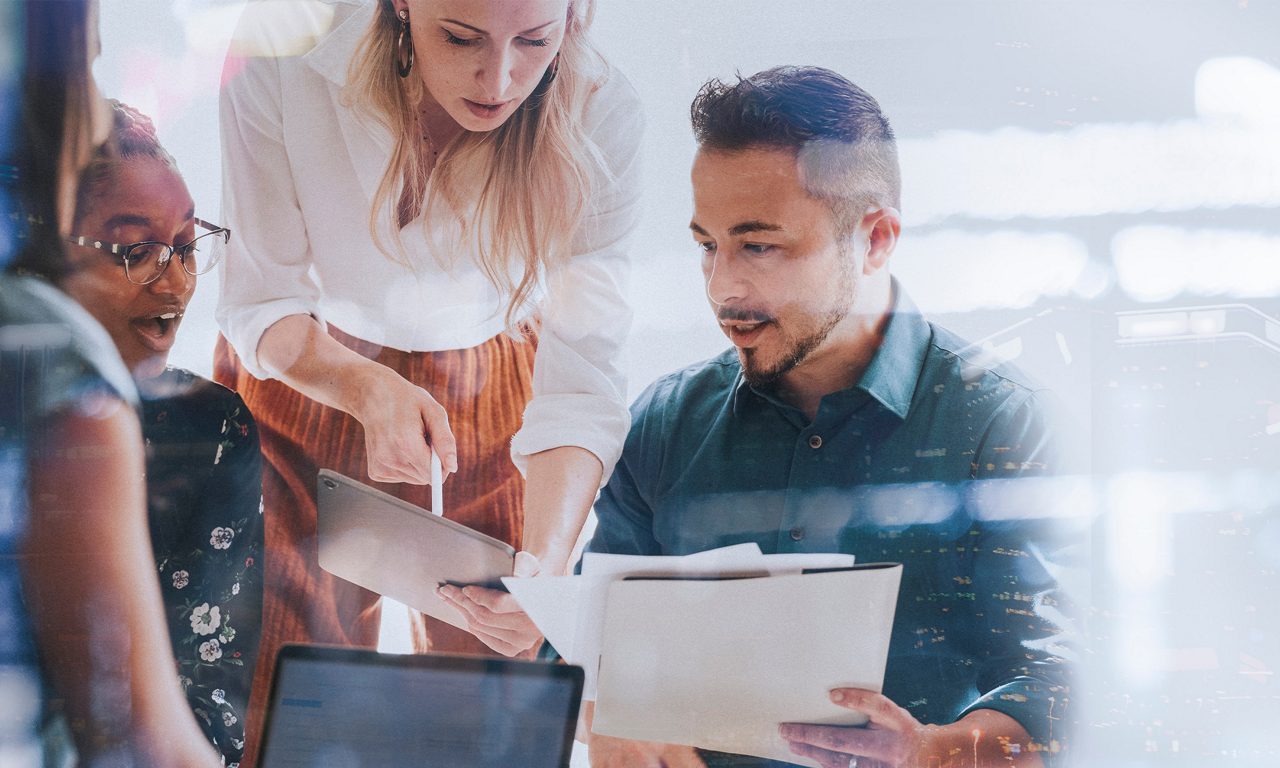 Fyra personer som sitter i möte runt ett bord och tittar på en iPad