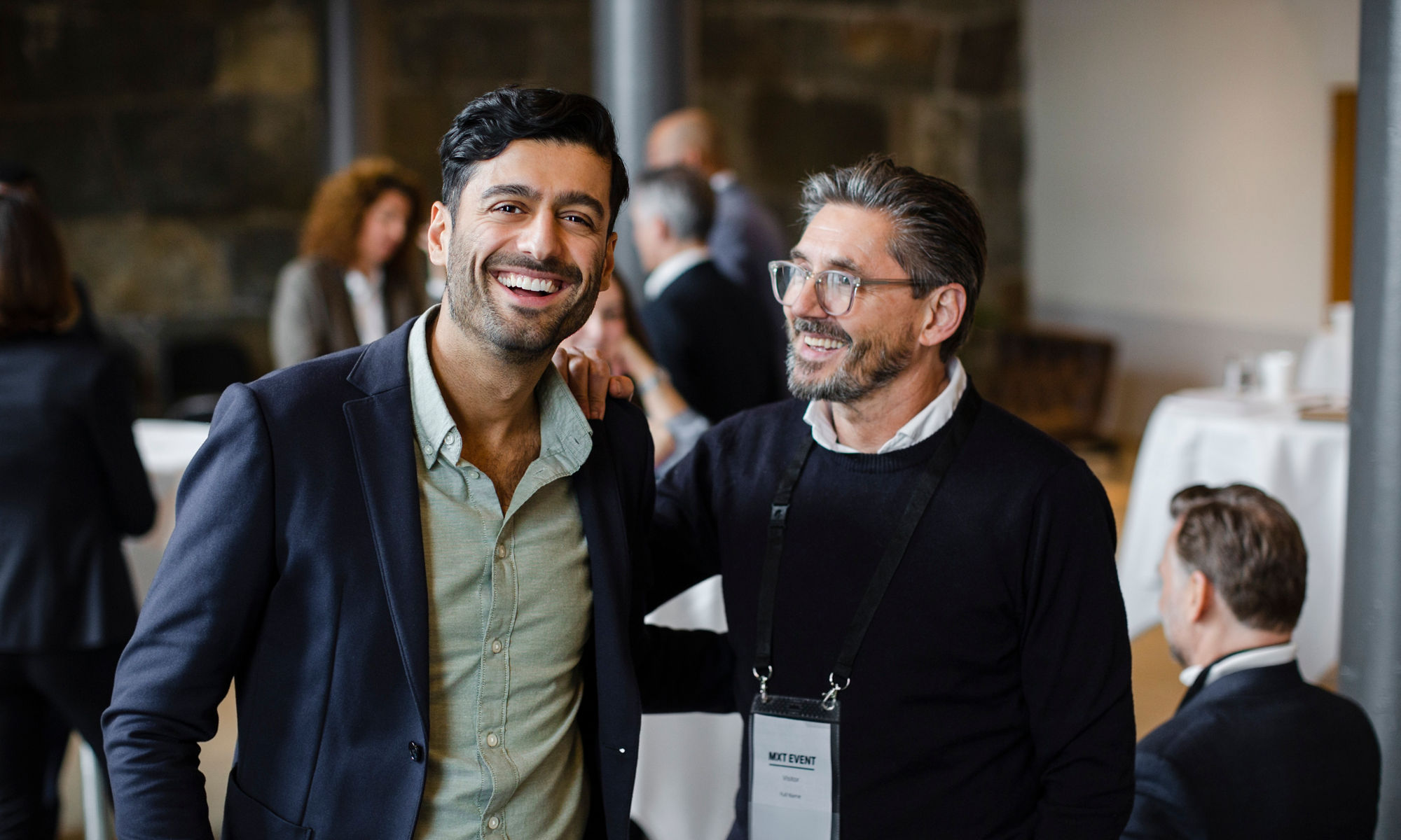 Two men at a business conference, smiling and hugging each other