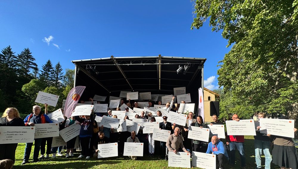 En stor grupp med människor står på och runt om en scen och håller upp checkar som de mottagit i utdelningen av Miljonen. 