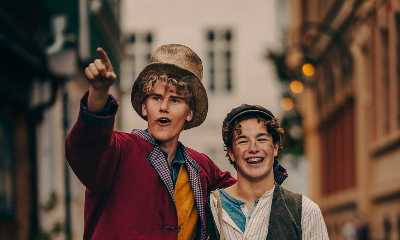 Två unga personer i kläder i vintagestil står nära varandra på en stadsgata.