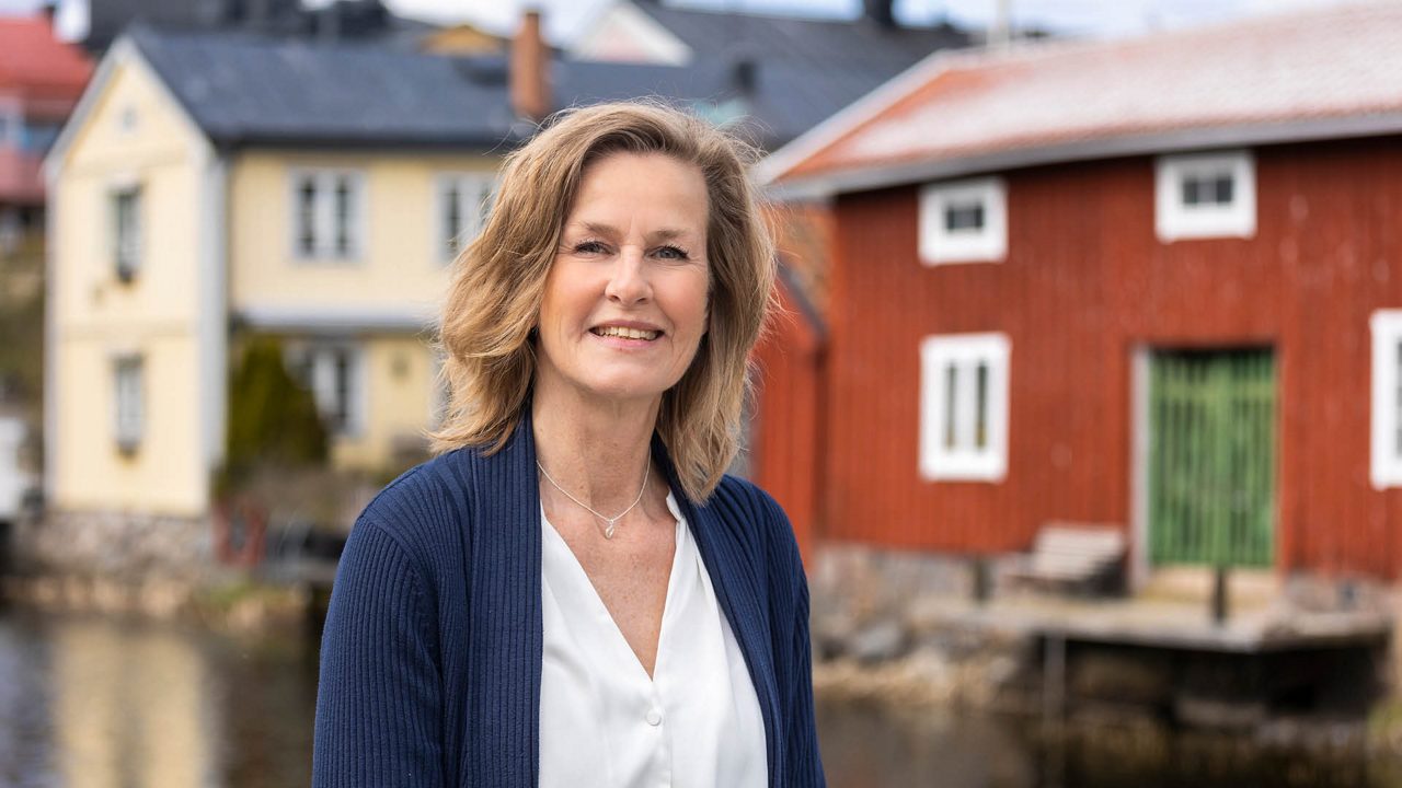 Petra är en av Roslagens Sparbanks premiumrådgivare. Med lång erfarenhet och ett stort engagemang möter hon kunderna med personlig rådgivning och skräddarsydda lösningar. På bilden står hon vid vattnet i en lokal miljö, med den röda träbebyggelsen i bakgrunden.